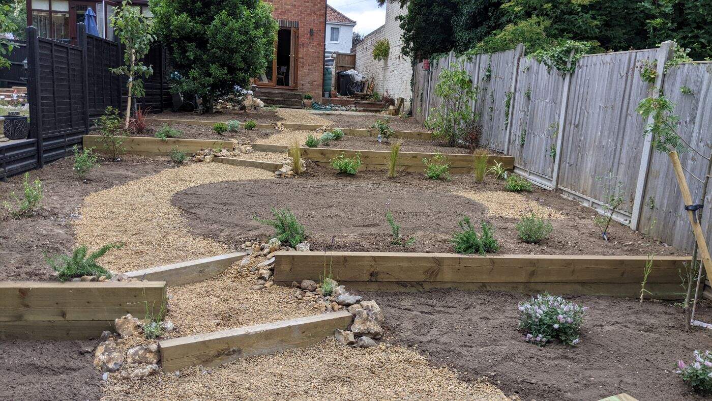 Contemporary Norfolk garden design with tiered plant beds and natural stone accents. Terraced garden immediately after installation showing sleepers and new planting